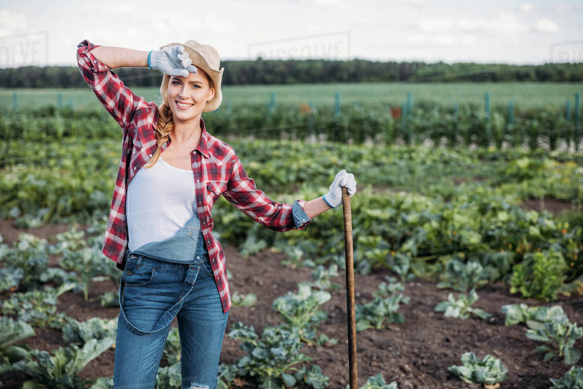 beautiful young female farmer in hat holding hoe and working on field - Farmer John Sausage Where To Buy